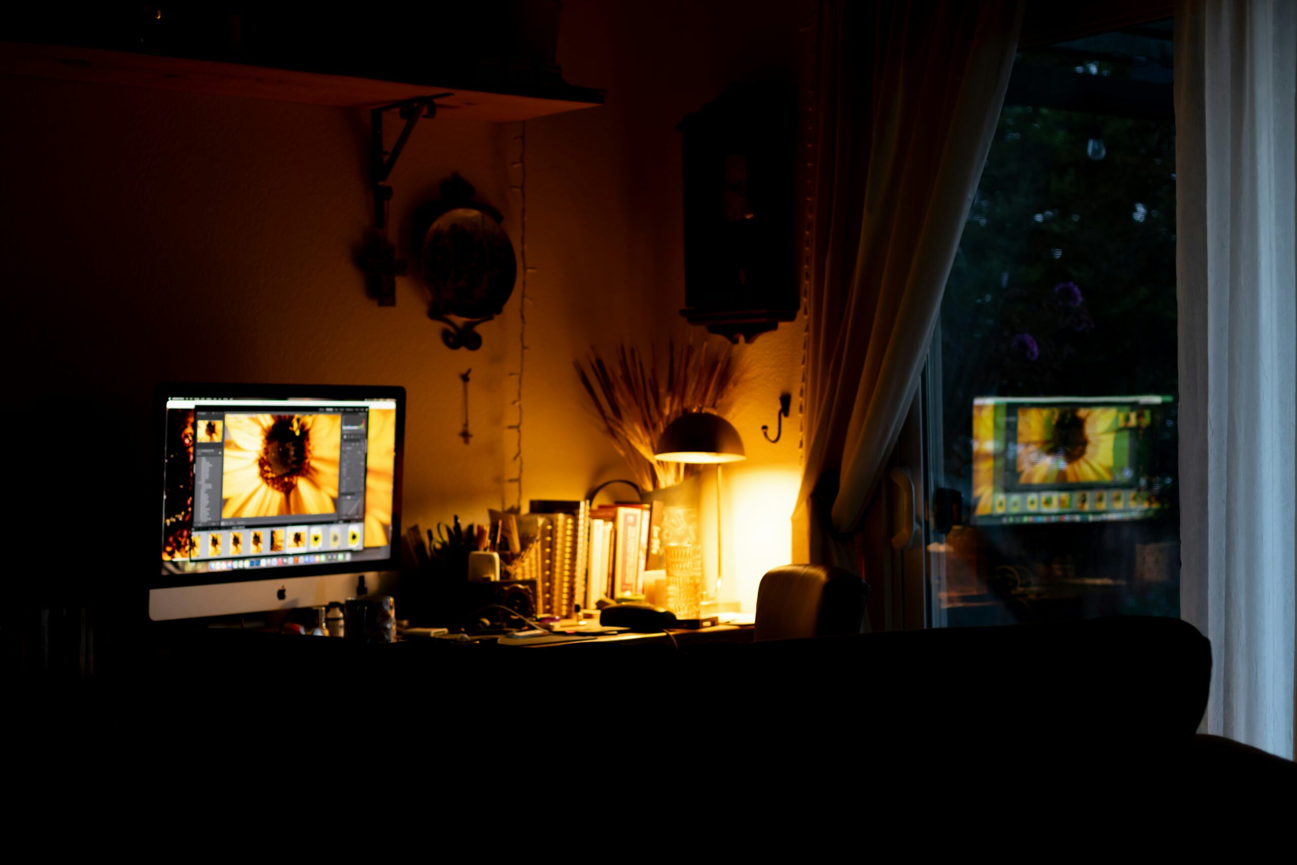 A dimly lit room with a computer and window reflection.